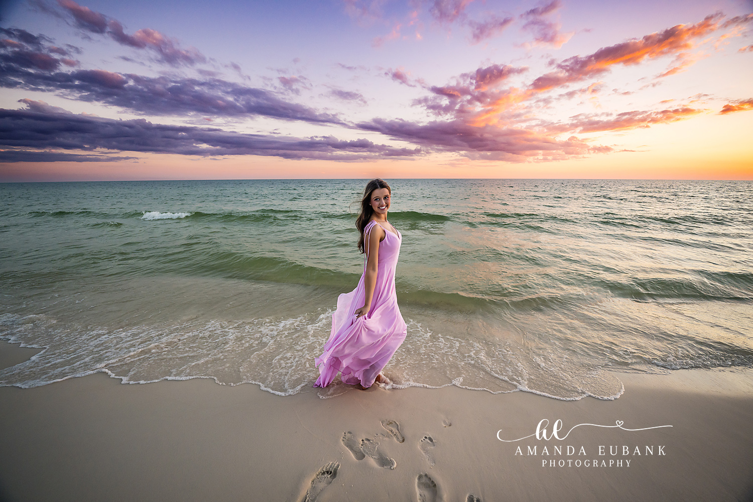 Lavender Gown at the Shore — Tampa Bay Senior Photography A senior in a lavender gown standing at the shoreline under violet clouds at a beach senior session in Tampa, FL.