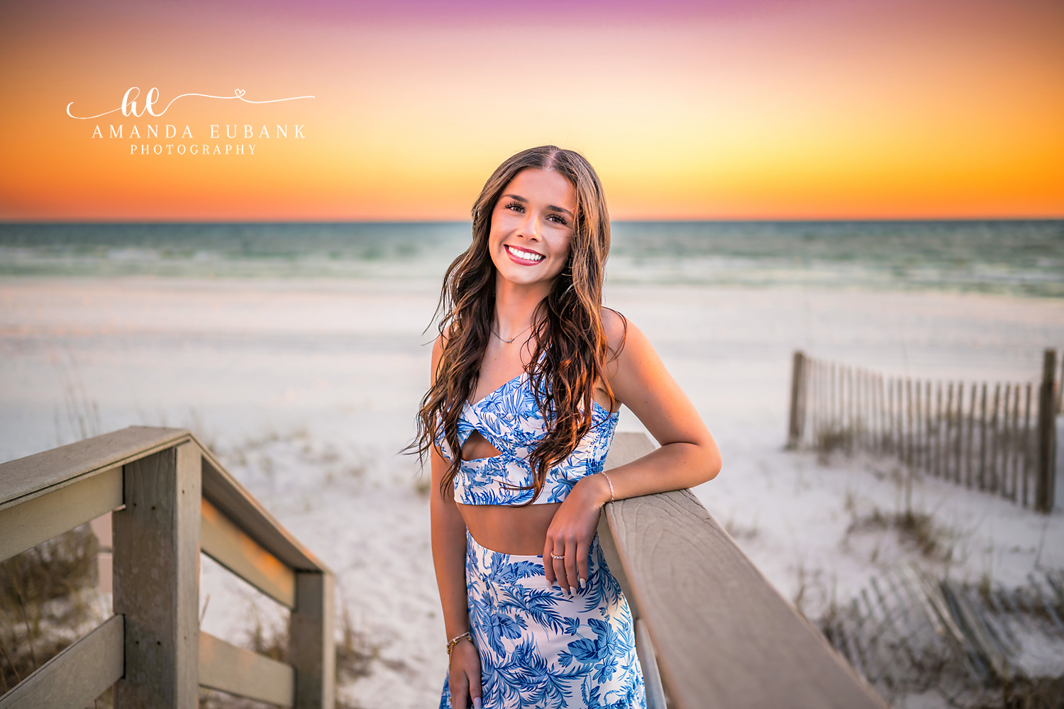 Leaning on the Dune Walkover | Tampa Senior Photographer A senior in a blue floral set leaning on a wooden dune walkover at sunset during a senior portrait session in Tampa, Florida.