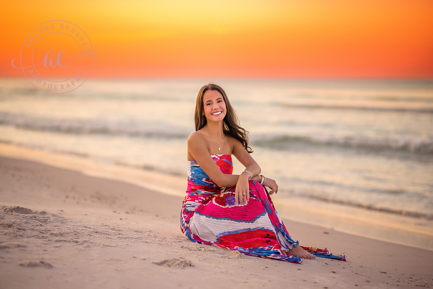 Seated Under an Orange Sky | Tampa Senior Photographer A senior in a pink skirt seated on the sand as the sky burns orange during a senior portrait session in Tampa, Florida.