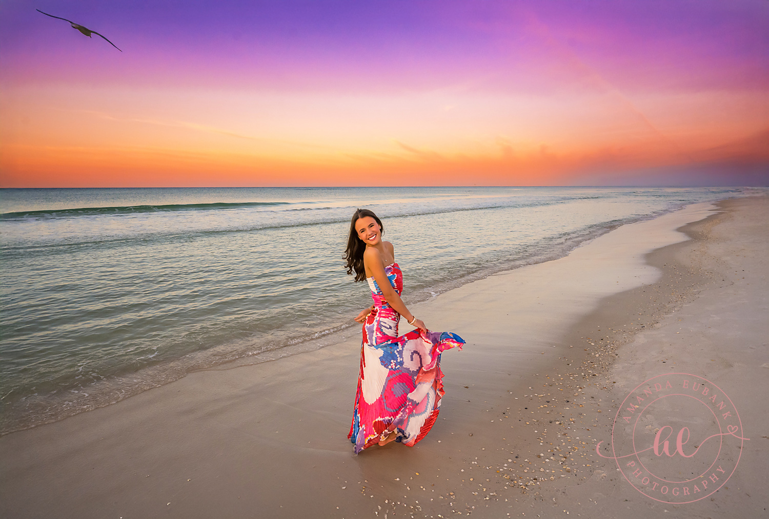 Pink Gown Under a Violet Sky — Tampa Bay Senior Photography A senior in a bright pink gown on the shoreline beneath violet and orange light at a beach senior session in Tampa, FL.