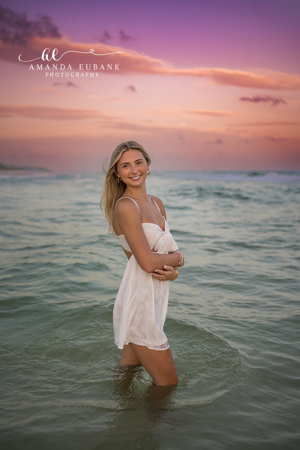 Standing Knee-Deep at Dusk | Beach Senior Session in Tampa, Florida Senior pictures in Tampa Bay showing a senior in a white dress standing knee-deep in the Gulf under a mauve sky.