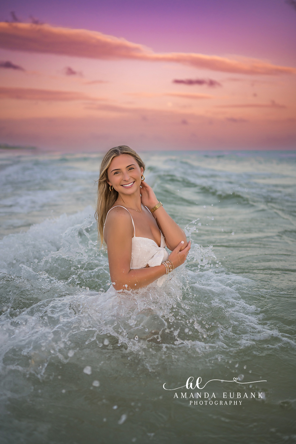 Wave Break Behind Her | Tampa Senior Photographer A senior in a white dress in the surf as a wave breaks white behind her during a senior portrait session in Tampa, Florida.