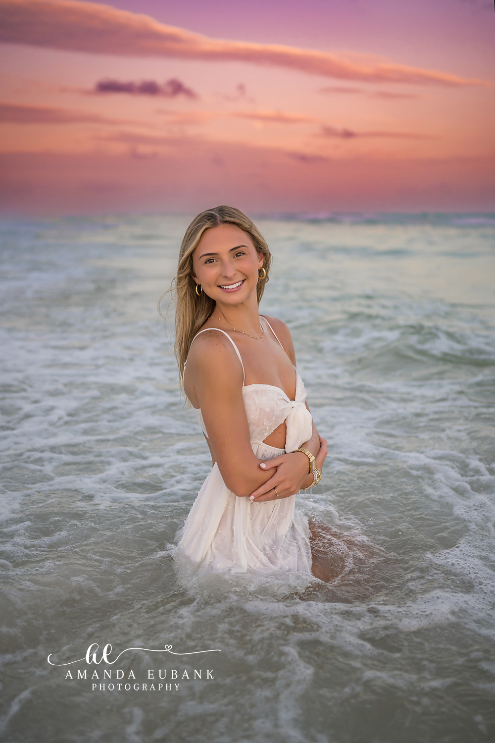 White Dress in the Waves — Tampa Bay Senior Photography A senior in a white dress in the breaking waves beneath a soft pink sky at a beach senior session in Tampa, FL.