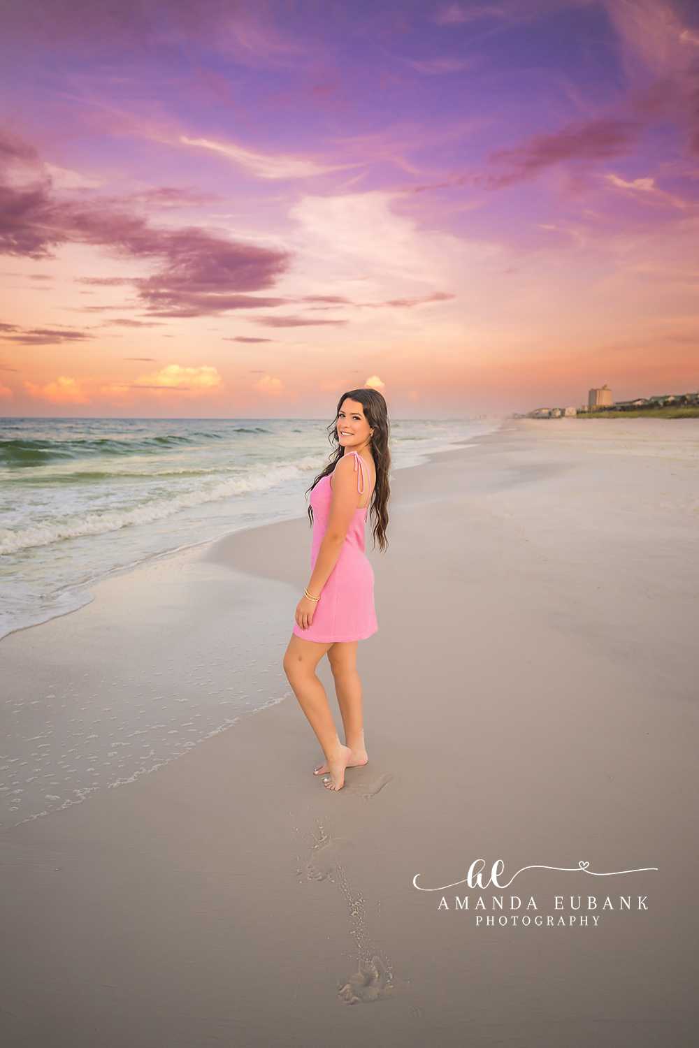 Pink Dress Under Violet Clouds | Tampa Senior Photographer A senior in a pink dress on the shoreline beneath violet and coral clouds during a senior portrait session in Tampa, Florida.