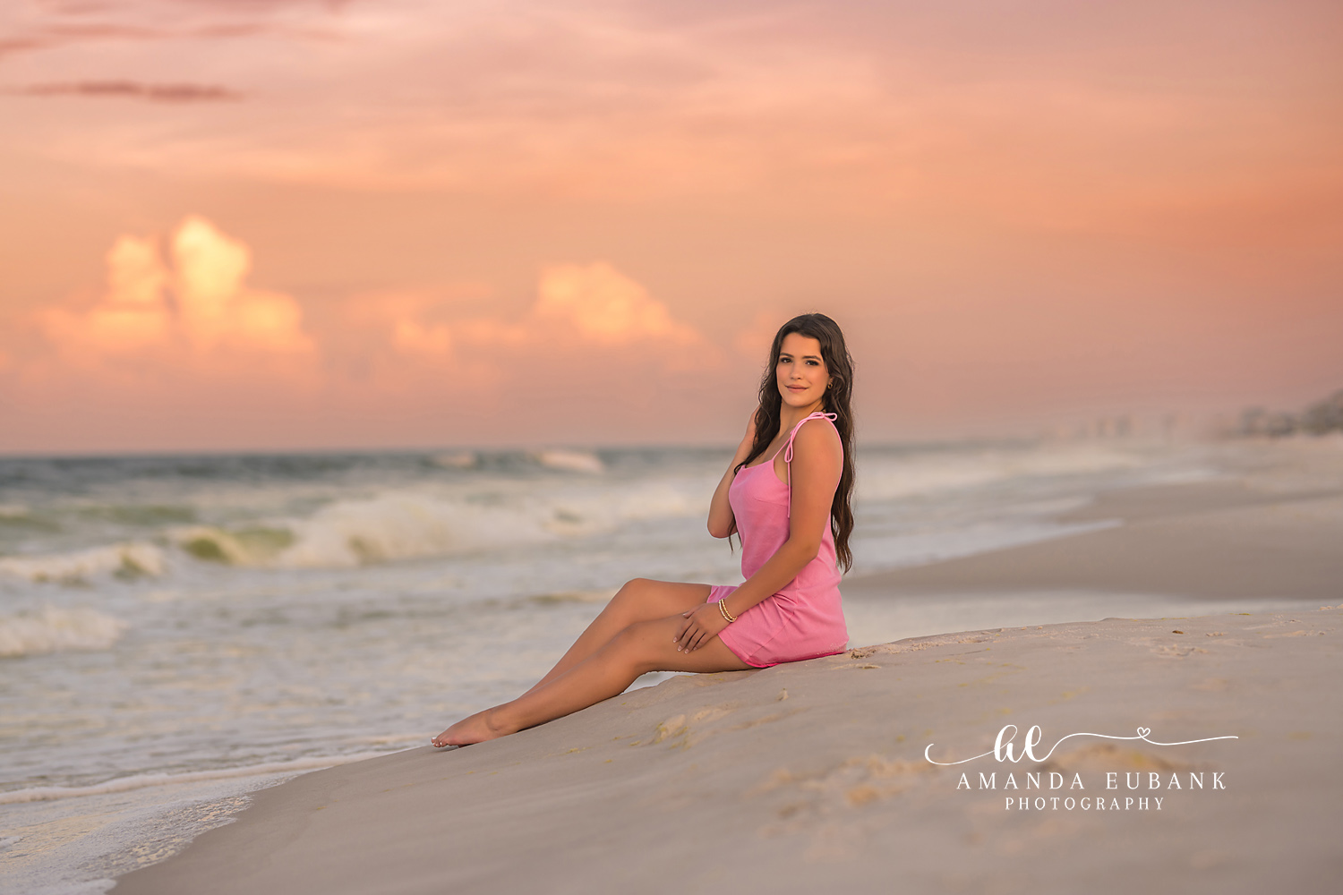 Pink Dress Seated on the Sand | Senior Portraits in Tampa, FL Tampa senior photographer captures a senior in a pink dress seated on the sand beneath soft peach clouds.