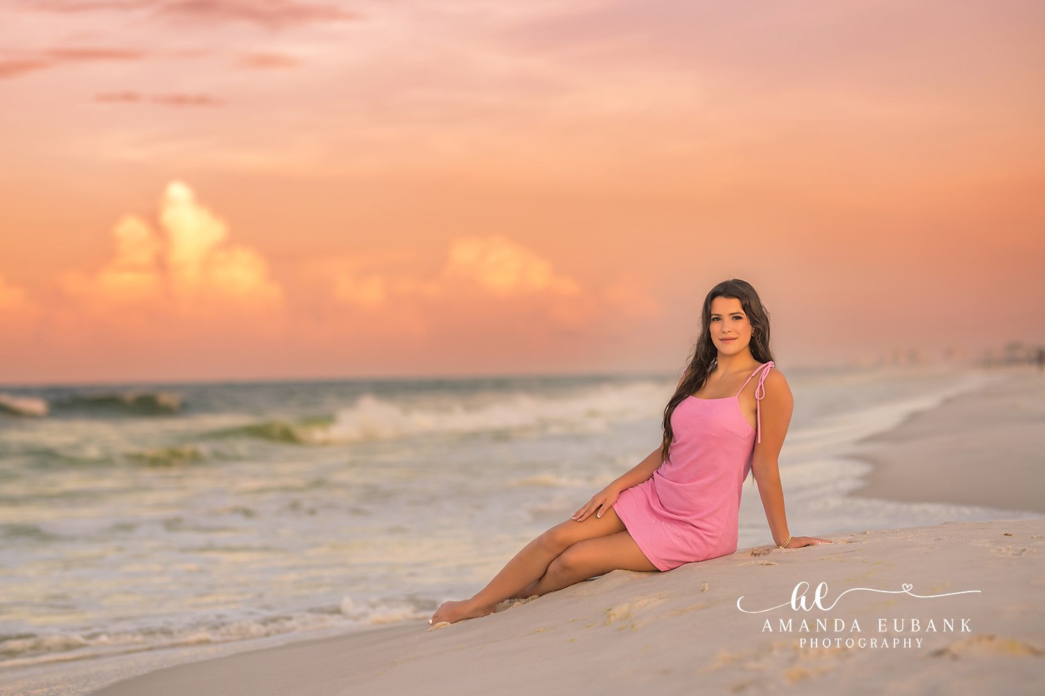 Peach Sky Senior Portrait — Tampa Bay Senior Photography A senior in a pink dress seated on the shoreline under a peach-toned sky at a beach senior session in Tampa, FL.