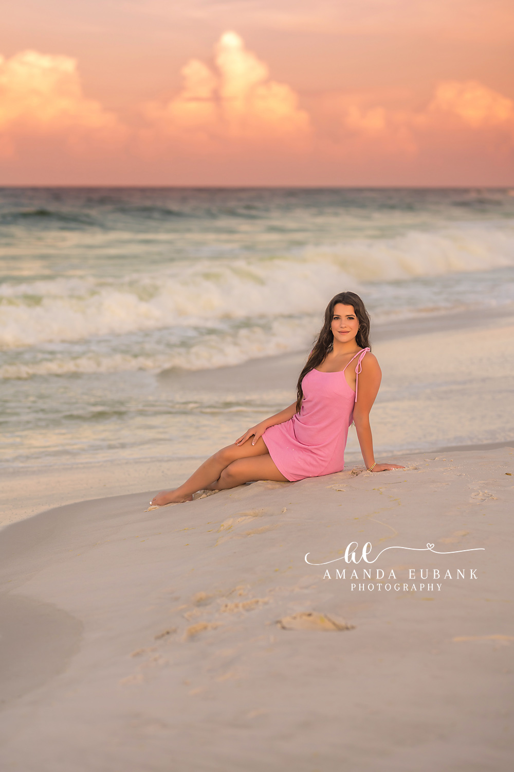 Seated by the Emerald Water | Beach Senior Session in Tampa, Florida Senior pictures in Tampa Bay showing a senior in a pink dress seated on the sand beside the emerald Gulf.