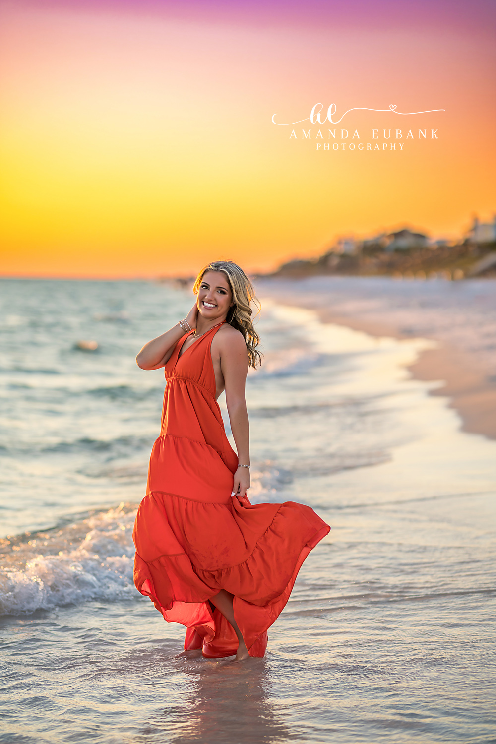 Red Gown at the Shoreline — Tampa Bay Senior Photography A senior in a flowing red gown standing at the shoreline at golden hour at a beach senior session in Tampa, FL.