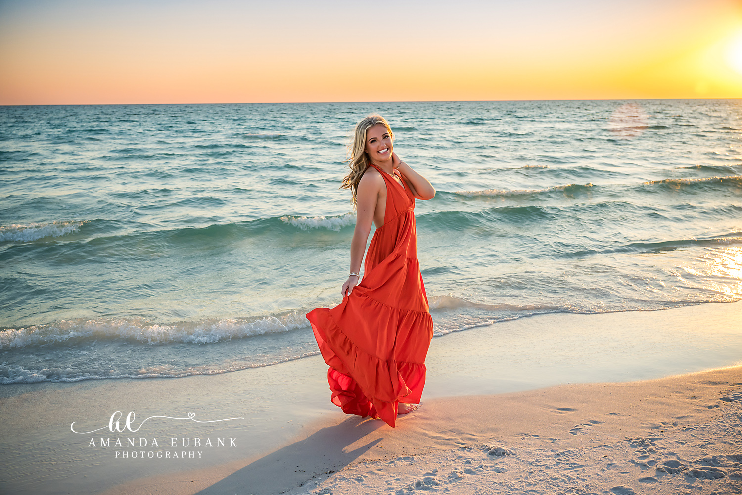 Red Gown at Sundown | Senior Portraits in Tampa, FL Tampa senior photographer captures a senior in a red gown on the shoreline as the sun sinks toward the water.