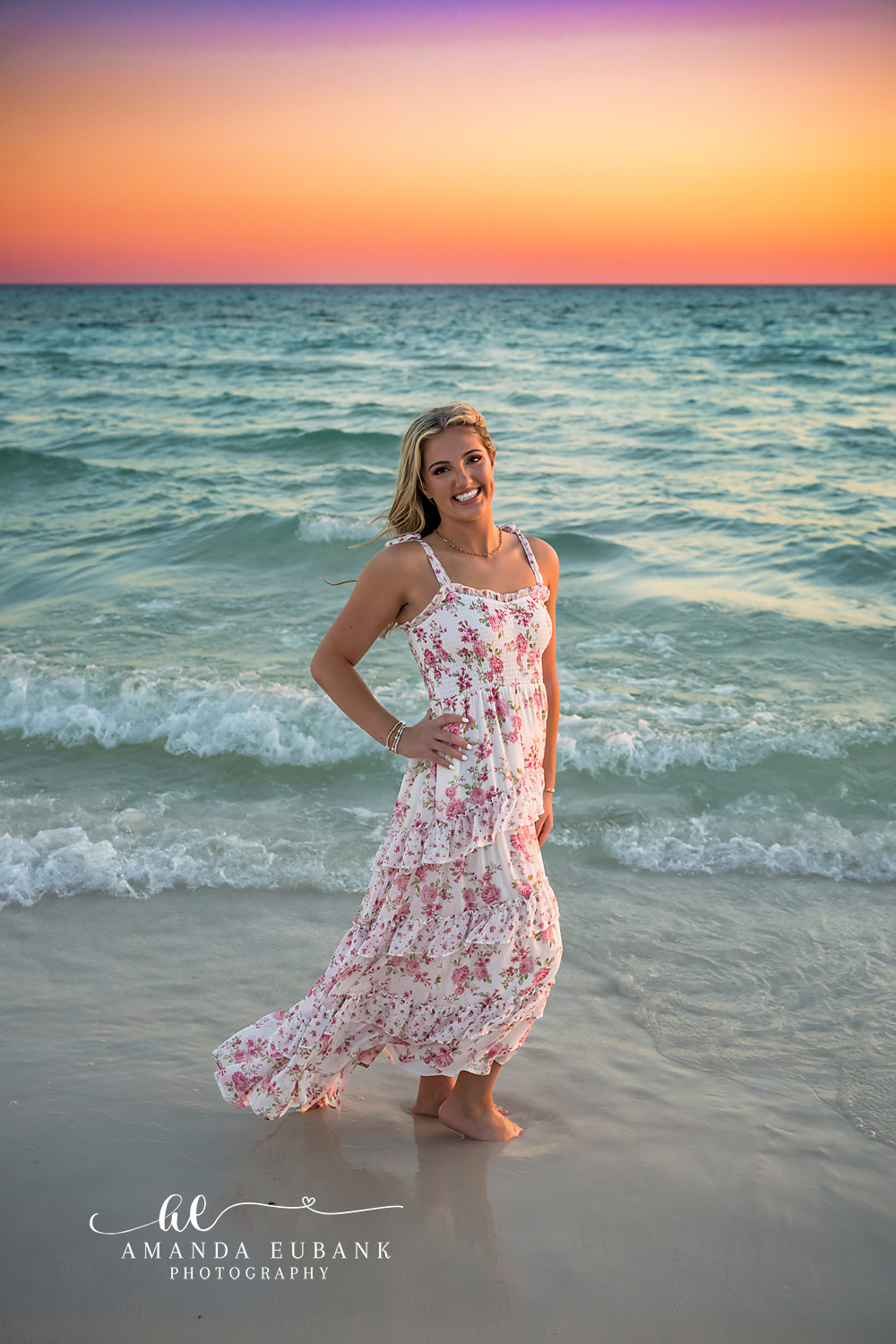 Floral Gown at Dusk | Beach Senior Session in Tampa, Florida Senior pictures in Tampa Bay showing a senior in a floral gown standing in the shallows as the sky turns coral.