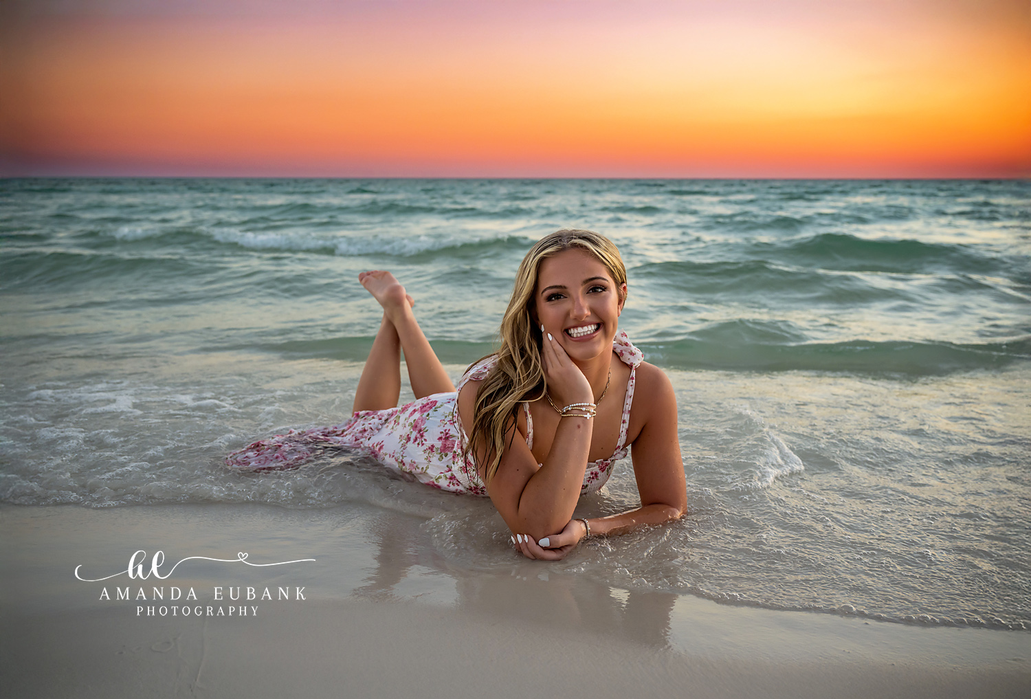 Lying on the Sand at Dusk | Beach Senior Session in Tampa, Florida Senior pictures in Tampa Bay showing a senior in a floral dress lying on the wet sand under an orange sky.