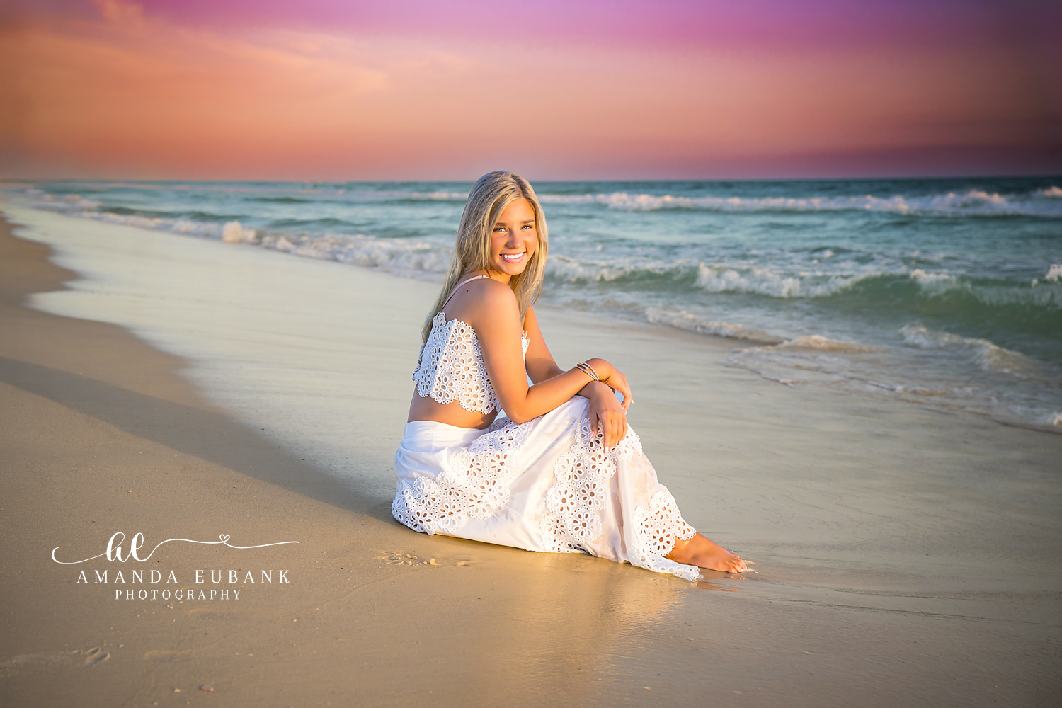 Seated in White on the Shore | Beach Senior Session in Tampa, Florida Senior pictures in Tampa Bay showing a senior in a white two-piece seated on the shoreline under a rose sky.