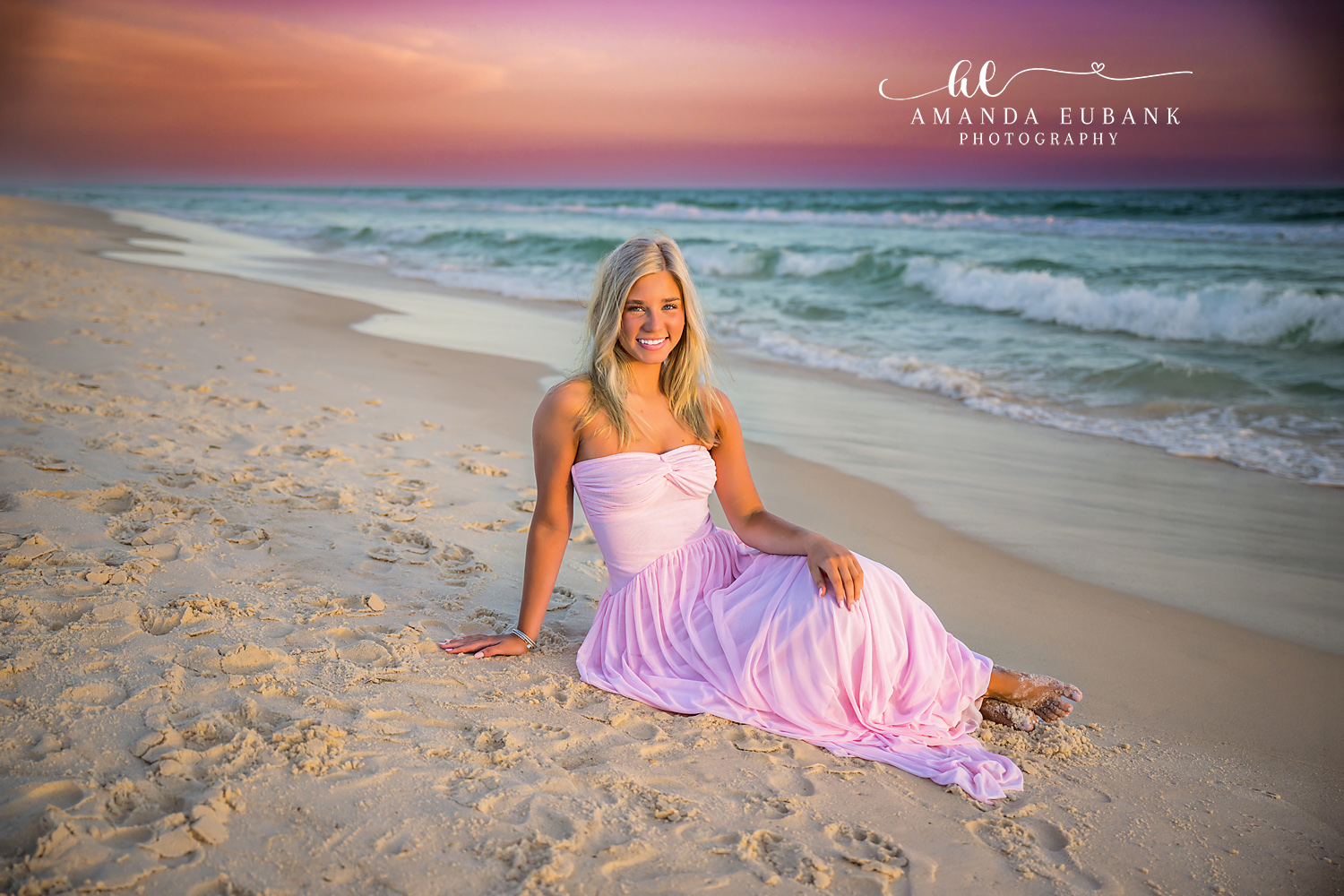 Lavender Gown on the Sand | Senior Portraits in Tampa, FL Tampa senior photographer captures a senior in a lavender gown seated on the sand beneath a rose and teal sky.
