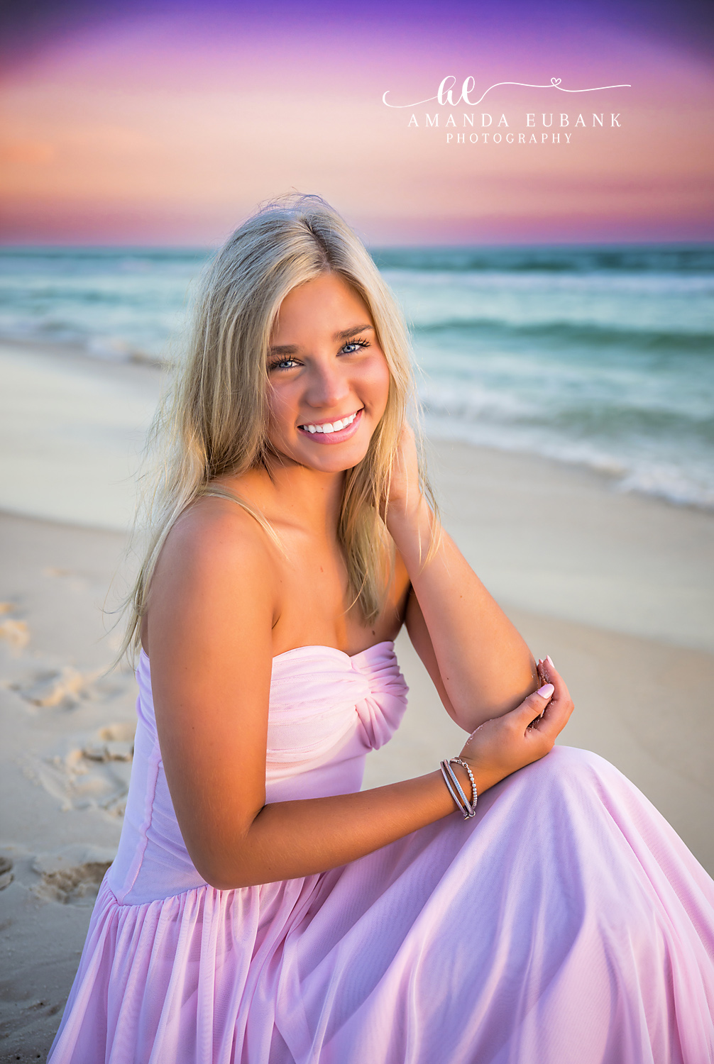 Lavender Gown Portrait on the Sand | Beach Senior Session in Tampa, Florida Senior pictures in Tampa Bay showing a senior in a lavender gown seated on the sand smiling toward the camera.