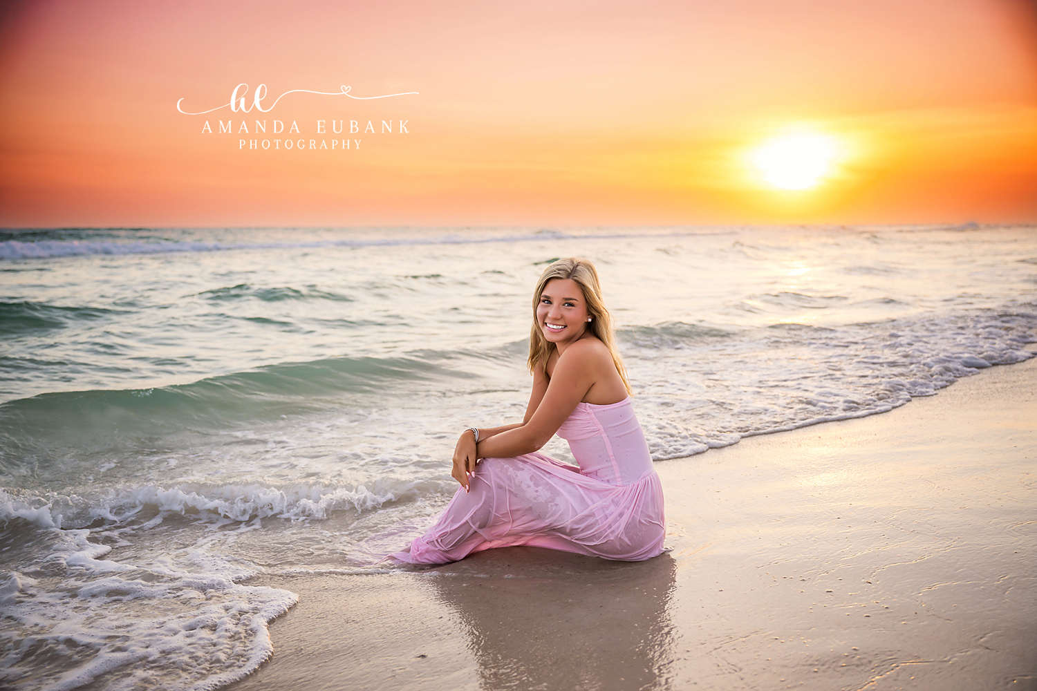 Seated in Pink at Sundown | Tampa Senior Photographer A senior in a pink gown seated on the shoreline as the sun meets the water during a senior portrait session in Tampa, Florida.