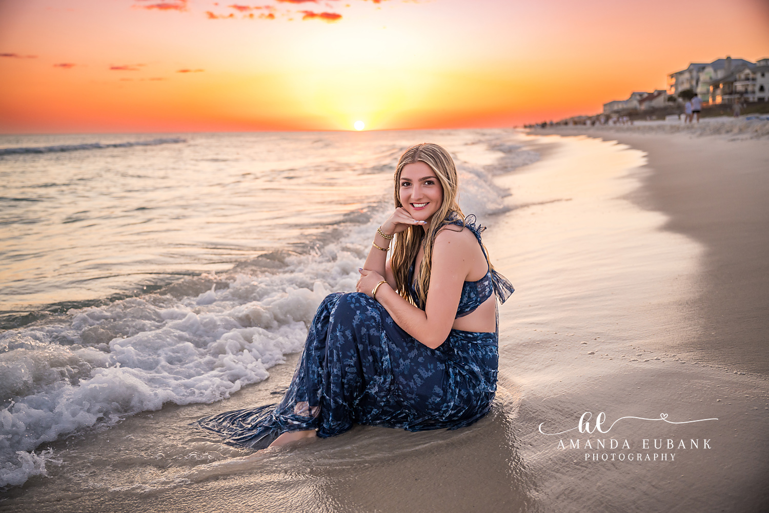 Navy Two-Piece in the Surf — Tampa Bay Senior Photography A senior in a navy two-piece seated in the surf as the sun sets behind the coast at a beach senior session in Tampa, FL.