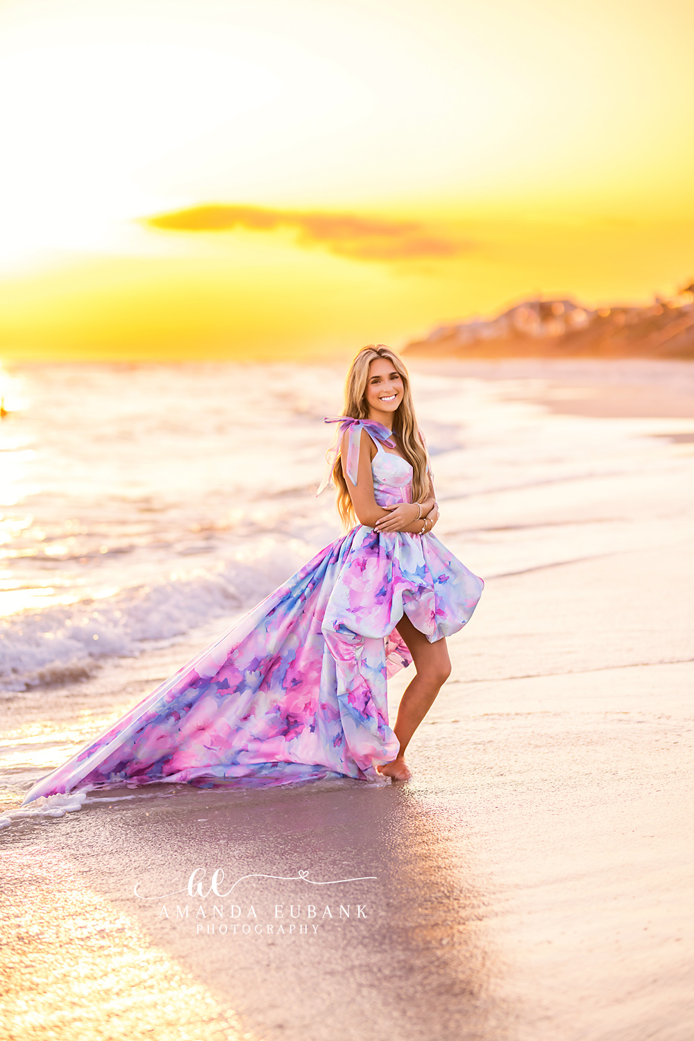 Printed Gown on the Shoreline | Tampa Senior Photographer A senior in a printed gown standing at the shoreline in warm golden light during a senior portrait session in Tampa, Florida.