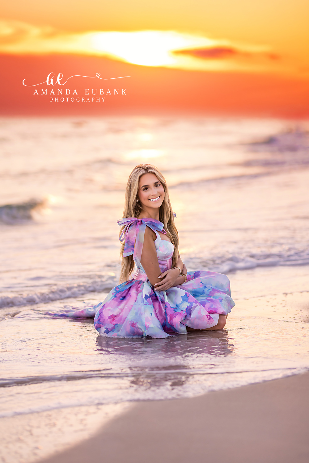 Printed Gown at Pastel Sunset — Tampa Bay Senior Photography A senior in a printed gown seated on the sand beneath a pink pastel sky at a beach senior session in Tampa, FL.