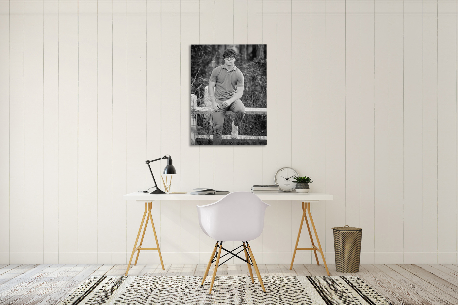 Black and white canvas of a senior guy seated on a wooden fence, displayed above a white desk