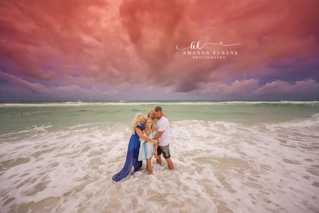 A couple embracing in the surf foam beneath dramatic magenta clouds, photographed by a Treasure Island engagement photographer